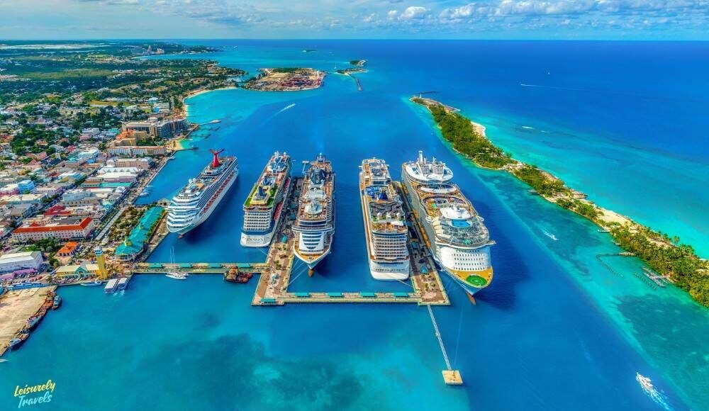 A stunning aerial view shows luxury cruise ships docked in clear turquoise waters near tropical islands. The white-sand beaches and vibrant blue ocean create a peaceful, dreamy atmosphere. It’s the perfect warm-weather escape for couples seeking relaxation and unforgettable moments.